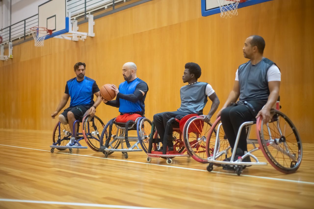 A diverse wheelchair basketball team practicing together on an indoor court.